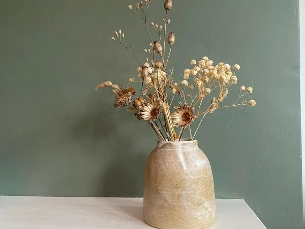 Handmade clay vase with dried flowers against a sage green wall