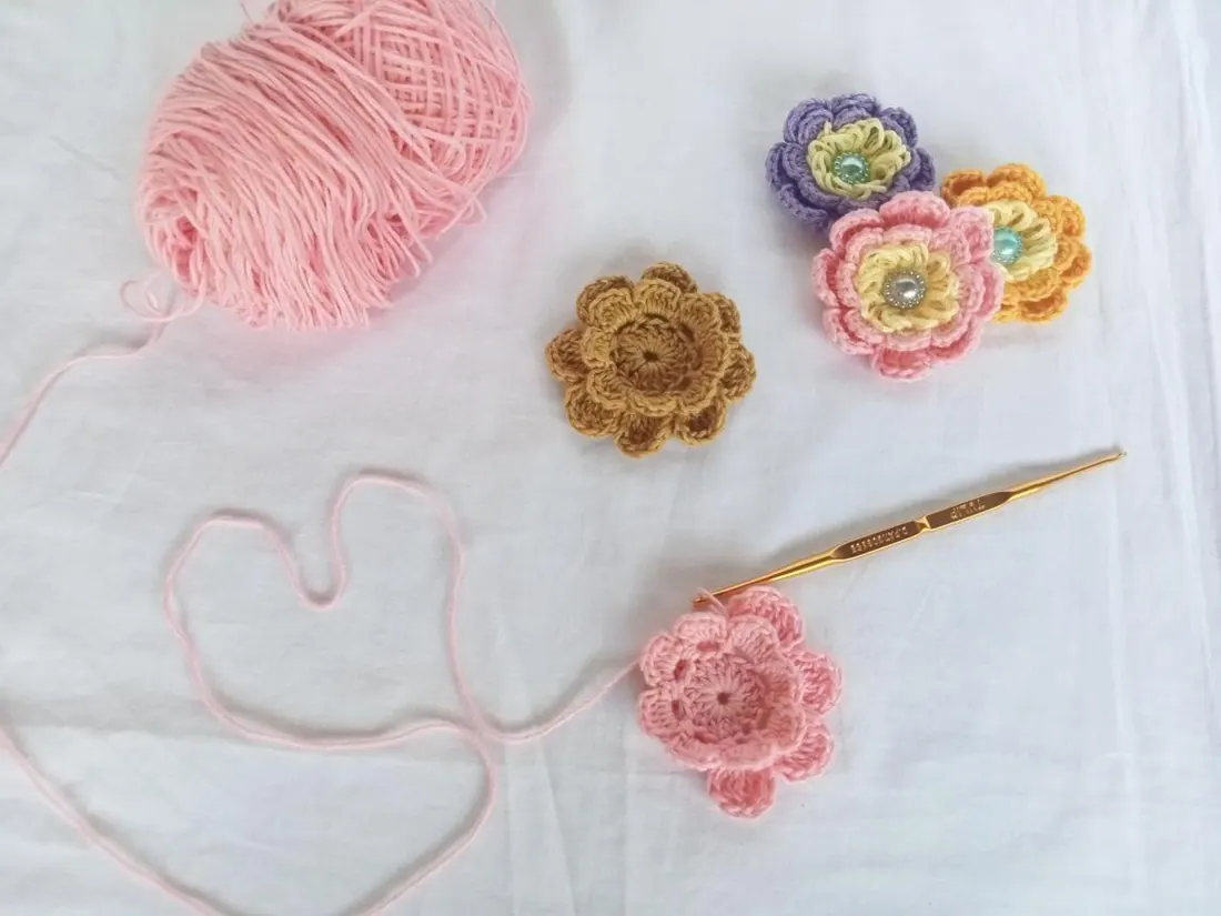 Crochet flowers with pink yarn and a gold crochet hook
